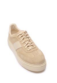 Beżowy zamszowy sneaker z fakturowaną cholewką, płaskimi sznurowadłami i kontrastowym jasnym paskiem. Gruba gumowa podeszwa, zaokrąglony przód.