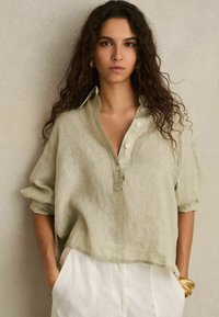Hellgrühes Leinenhemd mit langen Ärmeln, Knopfverschluss vorne und lockerer Passform. Verfügt über einen kleinen Kragen und aufgerollte Manschetten.