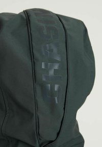 Sudadera de color verde oscuro con una textura suave, que presenta un destacado estampado gráfico negro de la palabra "CHASING" a lo largo del zipper.