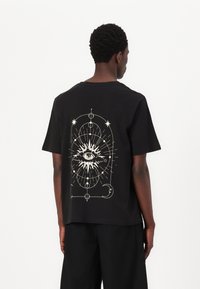 Black short-sleeve t-shirt featuring a white graphic of an eye surrounded by celestial elements on the back. Smooth cotton fabric.