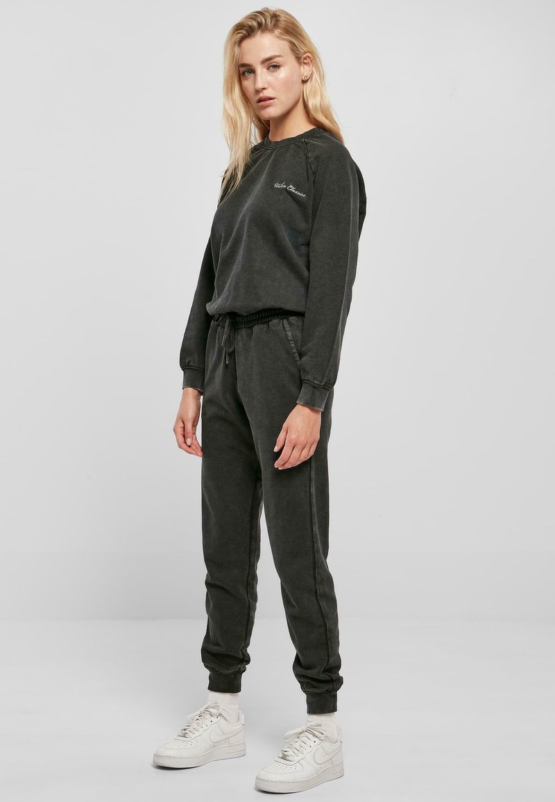 Mørkegrå bomullssweatshirt og matchende joggebukser med elastiske mansjetter, med et enkelt design og subtil merking på brystet. Hvite sneakers.
