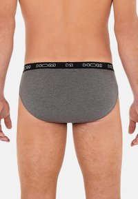 Grijze katoenen boxershort met een zwarte tailleband met witte "HOM" letters, ontworpen voor een strakke pasvorm en minimale bedekking.