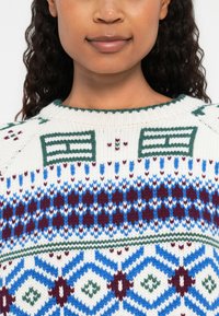 Maglione lavorato a maglia con base bianca, caratterizzato da motivi geometrici in blu, verde e bordeaux. Collo a coste e tessuto testurizzato.