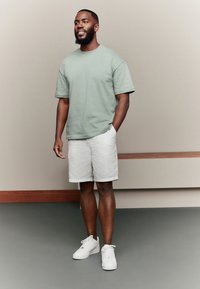 Lichtgroen katoenen T-shirt, witte linnen shorts en witte sneakers. Eenvoudig ontwerp met korte mouwen en een losse pasvorm.