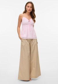 Light pink sleeveless top with lace trim and a tie front, paired with beige wide-leg pants, exhibiting a smooth, textured fabric.