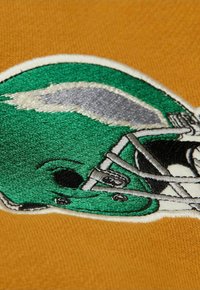 Casco da football verde ricamato su un tessuto arancione strutturato, con accenti grigi e dettagli neri, modellato in un design arrotondato.
