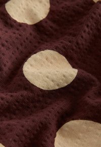 Close-up of textured brown fabric with large beige polka dots, showing knit pattern and soft, slightly wrinkled surface.
