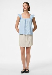 Blusa azzurra chiara con maniche a volant, abbinata a una mini gonna beige. La blusa presenta un collo quadrato e un tessuto morbido. Scarpe nere senza lacci.