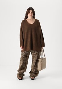 Brown knitted sweater with a V-neck, paired with loose leopard-print pants; carrying a beige handbag. Smooth texture; relaxed fit.