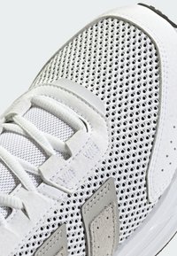 White sneaker featuring mesh upper, suede accents, and rubber sole. Includes lace details and grey overlays with perforations for ventilation.