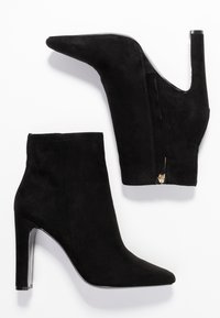 Par de botas de ante negras hasta el tobillo con puntera afilada, tacones cuadrados altos y cremalleras laterales sobre un fondo blanco.