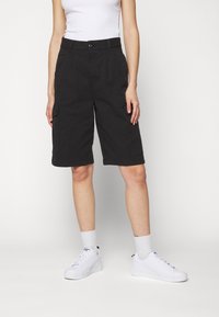 Shorts cargo noirs avec poches latérales, fermeture à bouton et coupe droite. Associés à des baskets blanches et des chaussettes de cheville.