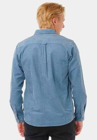 Camisa de pana azul claro con cuello recto, mangas largas y puños abotonados. Presenta una textura acanalada vertical y detalle de espalda con canesú.