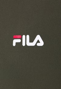 Ciemnooliwkowa tkanina o teksturowej powierzchni z białym logo FILA i małym czerwonym akcentem.