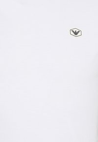 Vit bomulls T-shirt med en liten sexkantig logotyp i svart på övre vänstra sidan; slät textur och klassisk design.