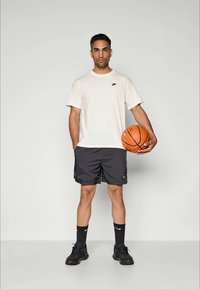 Nike creme t-shirt med et lille sort logo, sorte atletiske shorts, sorte sokker og sorte sneakers, mens han holder en orange basketball.