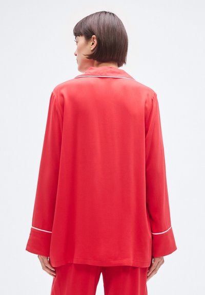 Červený pyžamový top s dlhými rukávmi vyrobený z hladkej látky. Obsahuje biely lem okolo goliera a manžiet. Neformálny strih s priamym strihom.