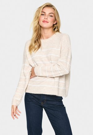 Lys beige striktrøje med hvide vandrette striber, rund halsudskæring og ribbede manchetter. Blød tekstur og afslappet pasform. Parret med mørke jeans.