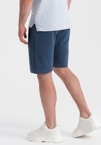 Bermudas azul marino de tela suave, con un corte relajado y bolsillos laterales, combinadas con zapatillas blancas gruesas.