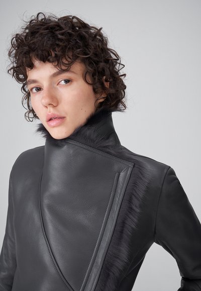 Chaqueta de cuero negra con cuello alto y detalles de piel, diseño asimétrico y texturas en el panel frontal.