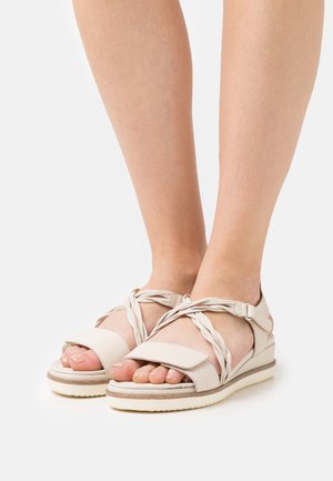 Light beige sandals with crisscrossed straps, soft leather upper, open toe, and rubber sole. Features include a cushioned footbed for comfort.