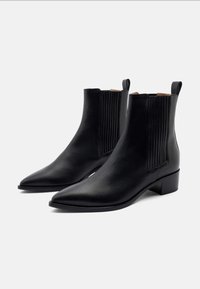 Botas de cuero negro hasta el tobillo con punteras puntiagudas, paneles laterales elásticos y un tacón bajo. Textura lisa y diseño minimalista.