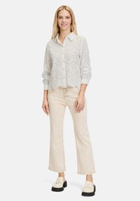 Hellbeige Bluse mit Lochmuster und langen Ärmeln, mit einer durchgehenden Knopfleiste, kombiniert mit beigen weit geschnittenen Hosen und klobigen schwarzen Slippern.