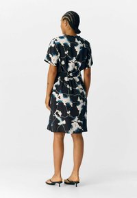 Robe noire ornée d'un motif floral bleu et blanc, à manches courtes, avec une taille nouée et une longueur jusqu'au genou. Texture lisse.