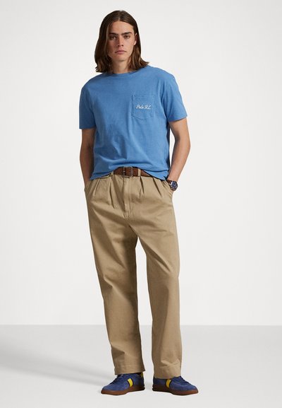 Tricou din bumbac de culoare albastru deschis, cu un buzunar pe piept, asortat cu pantaloni kaki cu croială lejeră. Purtați cu adidași albaștri cu accente galbene.