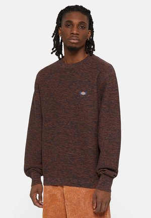 Sudadera de punto con motas marrones y naranjas, con cuello redondo y puños acanalados. Presenta un pequeño parche con logo en el pecho.