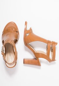 Beige korkokengät, jotka on valmistettu sileästä nahasta, pyöreällä kärjellä, leikkauksilla, kahdella hihnalla ja teksturoidulla puukorkokannan kanssa.