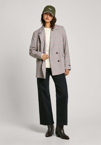 Blazer doppiopetto a quadri grigio chiaro, rosso e nero, abbinato a un maglione beige a girocollo e jeans larghi scuri. Stivaletti marroni.