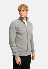 Szary, prążkowany sweter zapinany na zamek, z długimi rękawami i wysokim kołnierzem. Posiada teksturowany wzór dzianiny oraz dopasowany krój.