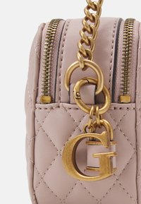 Borsa in pelle trapuntata rosa pallido con doppie zip, hardware in catena dorata e un grande charm a forma di "G" dorato. Dettaglio della superficie testurizzata.