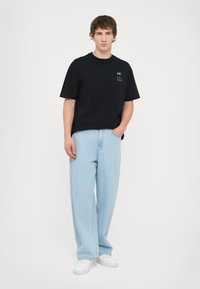 Černé tričko s krátkým rukávem a zlatými grafickými akcenty, kombinované s volnými světle modrými džínami a bílými teniskami. Jednobarevný a ležérní design.