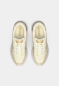 Λευκά αθλητικά παπούτσια με κρεμ λεπτομέρειες, λείο δερμάτινο πάνω μέρος, υφή στα πλαϊνά πάνελ και λευκά κορδόνια. Χρυσό λογότυπο στη γλώσσα. Παχιά, διάφανη σόλα.