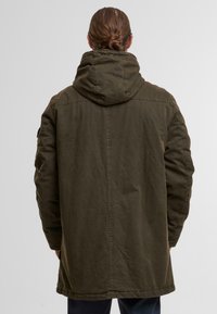 Olivgrüne Parkajacke mit Kapuze, die einen lässigen Schnitt, glatte Textur und kontrastierende Nähte entlang der Säume aufweist.