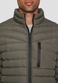 Graue Pufferjacke mit hohem Kragen, horizontalem Steppdesign, Frontreißverschluss und einer Reißverschlusstasche auf der linken Seite.