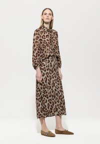 Langärmlige Bluse mit Leopardenmuster und passendem Rock in Beige- und Brauntönen; weicher Stoff mit glatter Textur; kombiniert mit Erdtönen-Slippern.