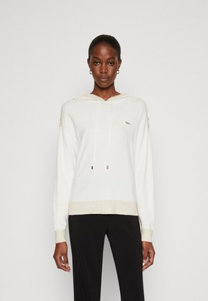Felpa bianca con cappuccio, dalla superficie testurizzata, con coulisse regolabile e un sottile logo dorato. Abbinata a pantaloni neri.