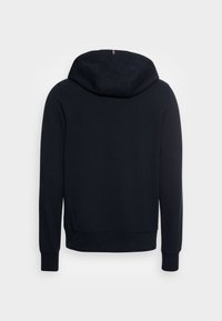 Sudadera negra con capucha espaciosa, puños y dobladillo acanalados. Presenta un sutil detalle en rojo y blanco en la costura de la capucha. Textura suave.