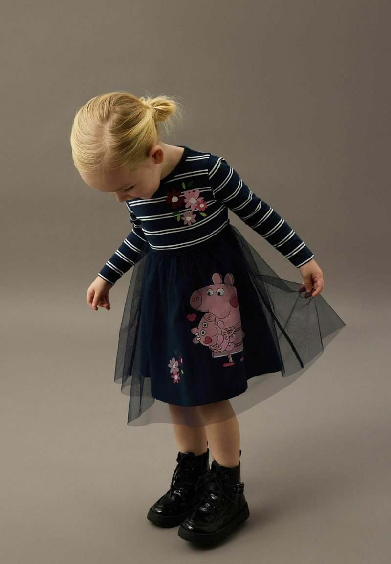 Granatowa sukienka z długimi paskowanymi rękawami, kwiatowym wzorem i tiulową spódnicą z motywem Peppy Pig. Całość dopełniają czarne buty za kostkę na sznurówki.