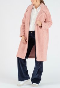 Roze, gestructureerde, overgrote jas met een gekarteld kraag, zijzakken en open voorkant. Gecombineerd met donkere corduroy broeken en witte sneakers.