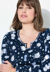 Granatowa koszula nocna o okrągłym dekolcie z wycięciem na kształt łezki. Wzór obejmuje koty, włóczkę i kwiaty w kolorze białym i jasnoniebieskim. Miękki materiał.