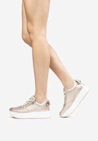 Sneakers metallic beige con una finitura liscia, design con lacci e una suola chunky bianca. Presentano un elegante pull tab sul retro e dettagli di cucitura.