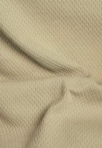 Beige strukturierter Stoff mit einem Waffelmuster, der weiche Falten zeigt. Das Material scheint atmungsaktiv zu sein und weist sichtbare Nähdetails auf.