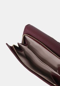 Portafoglio in pelle bordeaux con chiusura zip e molteplici scomparti, con un esterno texturizzato e un rivestimento interno beige liscio.
