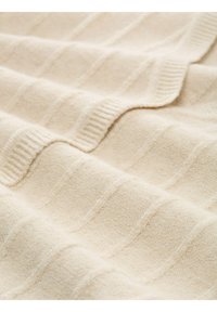 Pătură de culoare crem, cu un model texturat în forme de coaste, realizată dintr-un material moale, cu o strălucire subtilă și un aspect confortabil. Marginile texturate sunt vizibile.