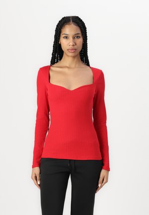 Red long-sleeve top with a square neckline, ribbed texture, fitted design, and smooth fabric. Worn with dark pants.