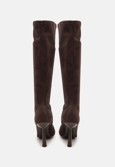 Paire de bottes hautes en daim marron foncé à talons hauts, vues de dos, debout sur un fond clair.